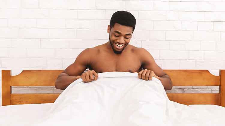 Excited african-american man looking at his body part under sheets