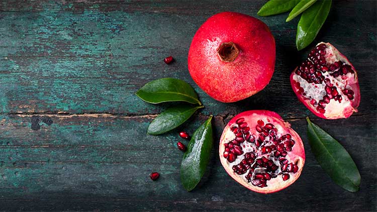 Fresh juicy pomegranate - whole and cut, with leaves on a wooden vintage background, top view, horizontal, with copy space