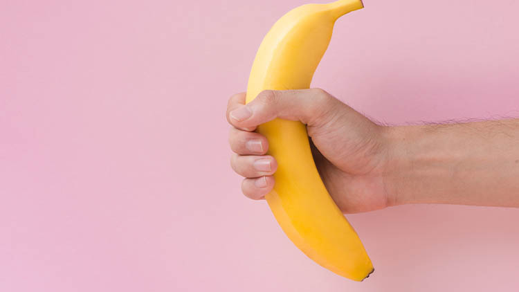 Male hand holding a banana isolated on pink background