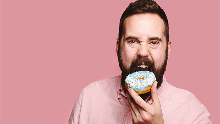 Sweet tooth - Hungry man taking a big bite of a blue donut, isolated on pink studio background