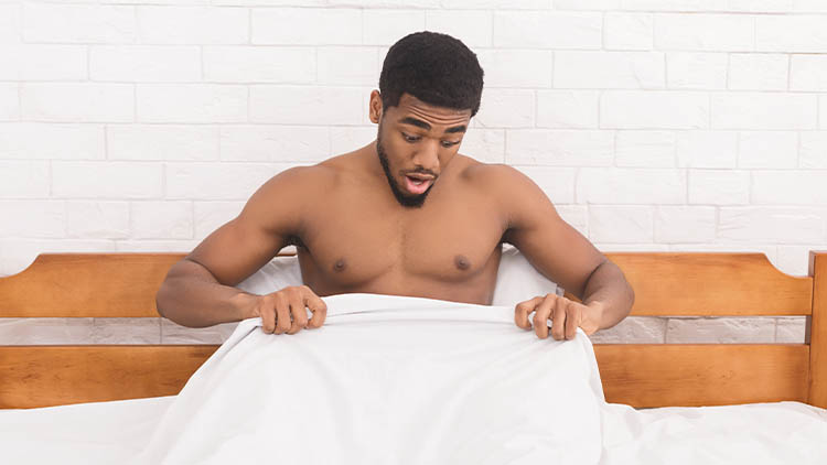 Young black man in bed looking at his penis