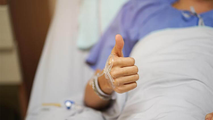 male patient holding a thumbs up while laying in the hospital bed