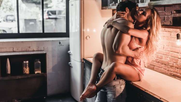Man kissing woman sat on kitchen counter intimately