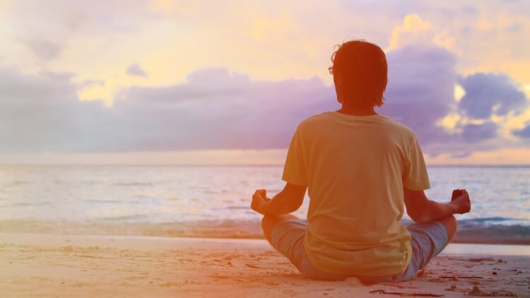 Young man meditating on beach at sunset